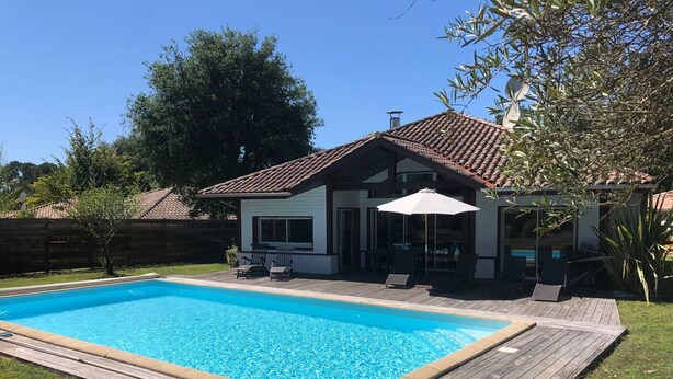 Ein Garten mit Swimmingpool, Holzterrasse und einem Haus mit Ziegeldach.