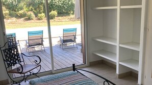 Ein Zimmer mit einem Bett, einem Fenster mit Blick auf Sitzgelegenheiten im Freien und einer weißen Regaleinheit.