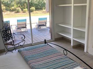 Ein Zimmer mit einem Bett, einem Fenster mit Blick auf Sitzgelegenheiten im Freien und einer weißen Regaleinheit.