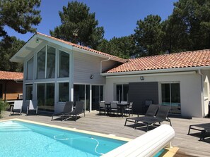 Ein modernes, zweistöckiges Haus mit Swimmingpool, Außenbereich mit Sitzgelegenheiten und einer großen, verglasten Terrasse.