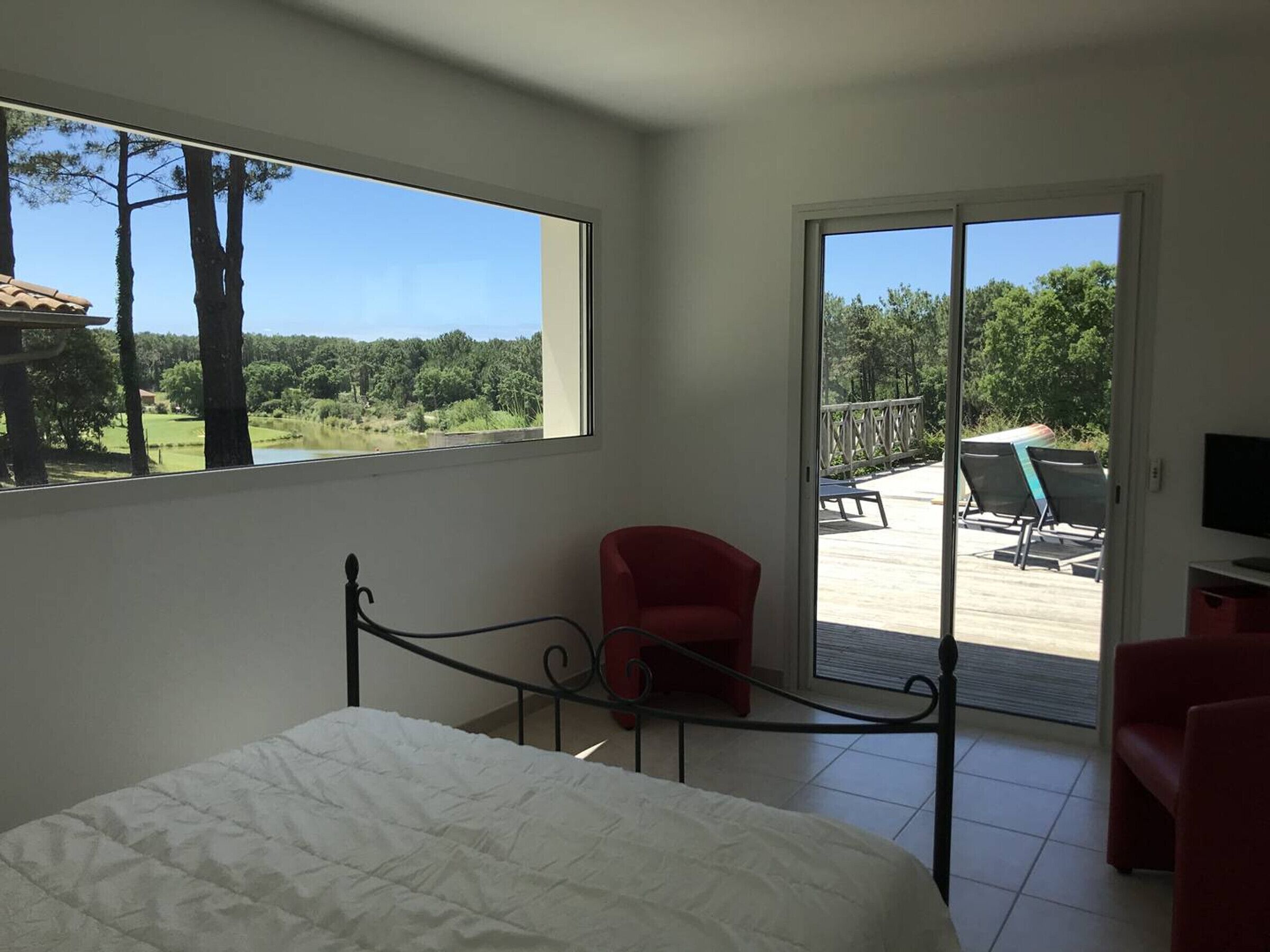 A bedroom with a bed, a red chair, and a balcony with outdoor furniture.