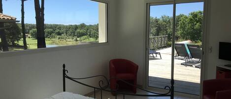 A bedroom with a bed, a red chair, and a balcony with outdoor furniture.
