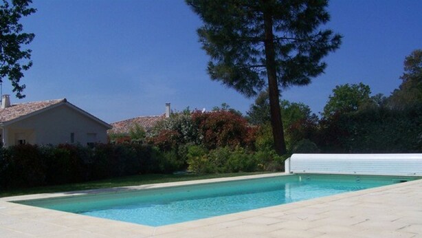 Ein rechteckiger Pool mit Fliesen umgeben, umgeben von Grünflächen und einem Haus im Hintergrund.