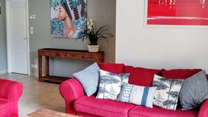 Ein rotes Sofa mit gemusterten Kissen, ein Holzkonsolentisch, ein Blumentopf und ein Bild an der Wand.