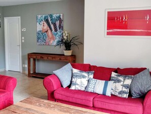 Ein rotes Sofa mit gemusterten Kissen, ein Holzkonsolentisch, ein Blumentopf und ein Bild an der Wand.
