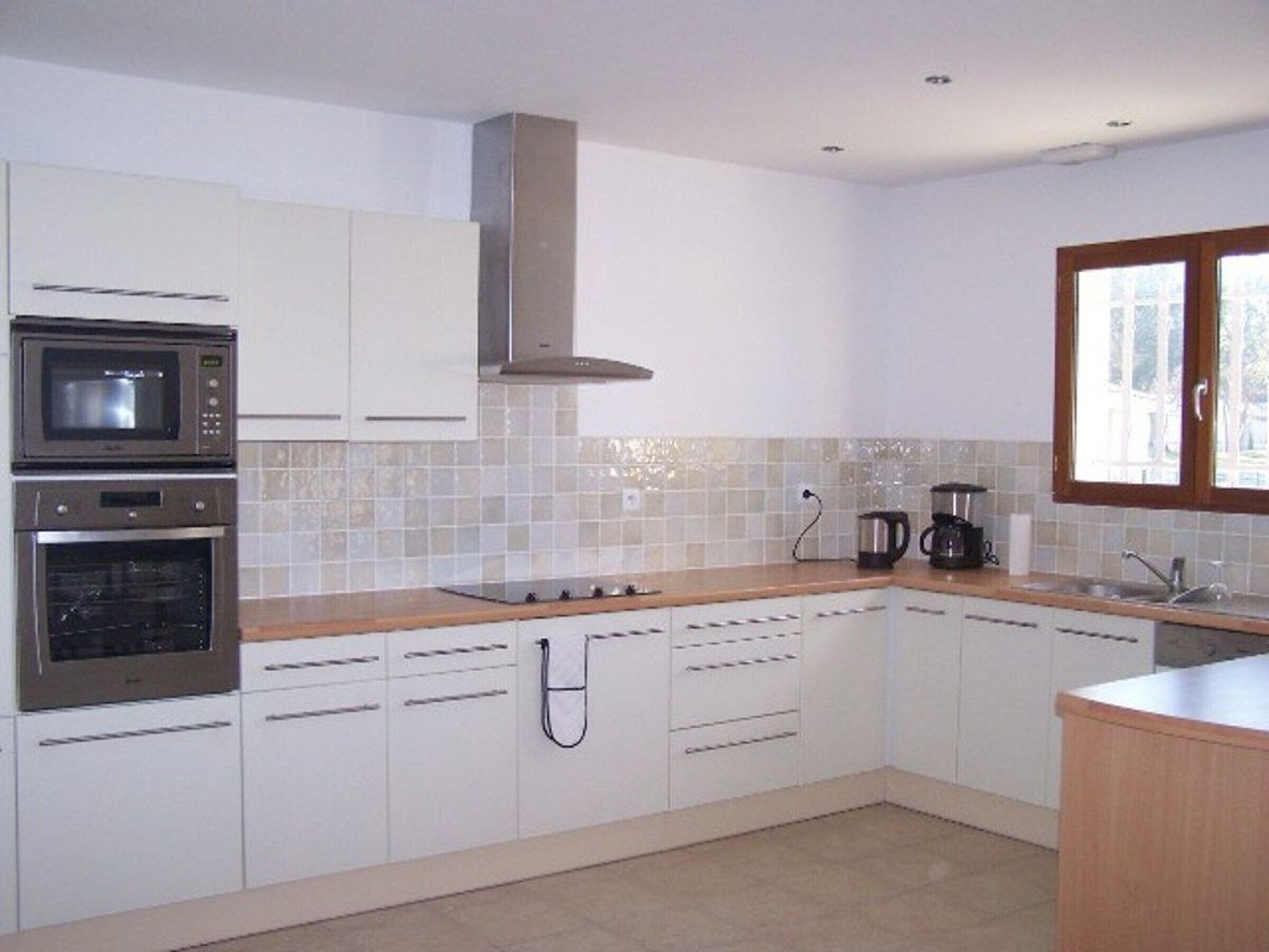 Una cocina moderna con armarios blancos, horno empotrado, microondas, estufa y ventana.