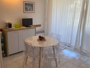 A compact kitchen with a dining area, a television, and a window with curtains. - Apartment with pool - 4 guests (Moliets-et-Maa)