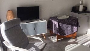 Ein kleiner, moderner Raum mit Fernseher, einem Esstisch mit Spitze-Tischdecke, einer Korbtasche-Lampe und einer Mikrowelle auf einem Regal.