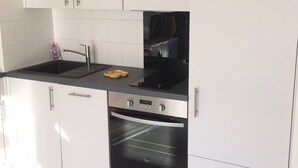 Eine Küche mit weißen Schränken, einer schwarzen Arbeitsplatte, einem Edelstahl-Spülbecken, einem Geschirrgestell und einem eingebauten Backofen.