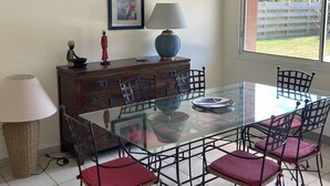 Un coin repas avec une table en verre, des chaises en métal, un buffet en bois, une lampe et un tableau encadré au mur.