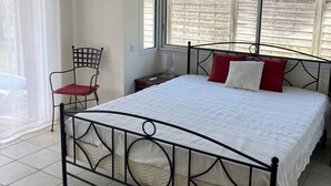 Une chambre à coucher comprenant un lit, une chaise, une table de chevet et une fenêtre avec des stores.