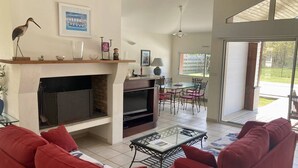 Un salon avec des canapés rouges, une cheminée, un coin repas avec des chaises et une grande fenêtre.