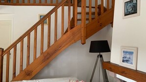Un escalier en bois dans une pièce où se trouvent un lit, une lampe et des tableaux encadrés accrochés au mur.