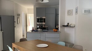 Une cuisine moderne avec des meubles gris, un four encastré et un coin repas comprenant une table et des chaises en bois.