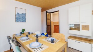 A dining area with a wooden table set for four, chairs, a small plant, and a wall-mounted artwork. - Family-friendly accommodation with terrace & garden (Tribalj)