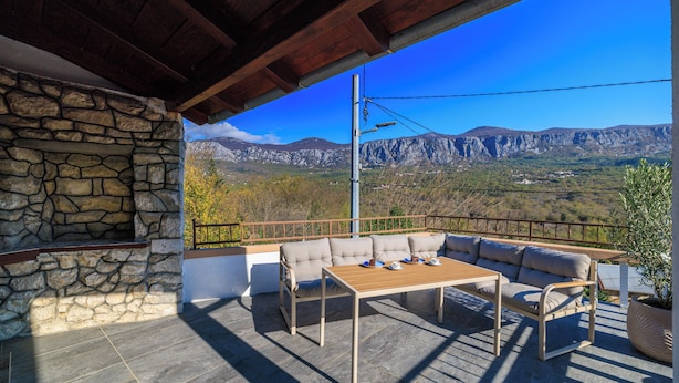 A stone wall, a wooden table, a beige sofa, and a view of mountains. - Family-friendly accommodation with terrace & garden (Tribalj)