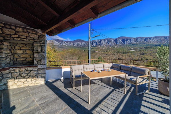 Eine Steinsäule, ein Holztisch, ein beiges Sofa und Blick auf Berge.