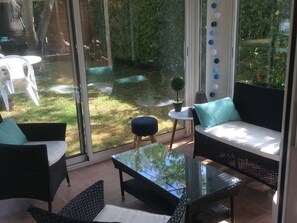 A modern outdoor seating area with wicker furniture, a glass table, and a view of a garden. - House with heated pool - 8 guests (Moliets-et-Maa)