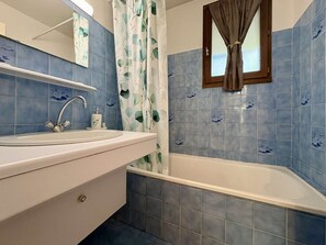 Een badkamer met een witte wasbak, een spiegel, een douchegordijn met bladmotief en blauwe betegelde wanden.