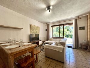A living room with a sofa, a TV, and a dining table set for four. - Spacious apartment with private garden - 6 guests (Le Monêtier-les-Bains)