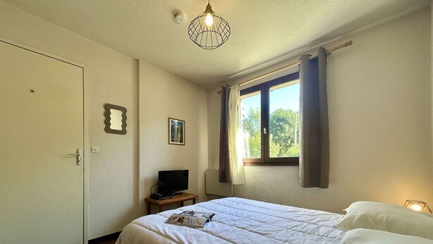 Una camera da letto con un letto, una televisione su un tavolino, una finestra con tende e una porta.