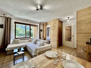 A room with a sofa, a dining table set for two, and a wooden wall with a heart decoration. - Spacious apartment with private garden - 6 guests (Le Monêtier-les-Bains)