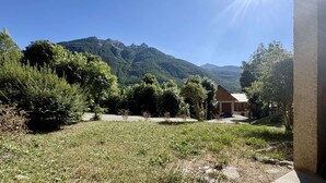 Una zona erbosa con un edificio e alberi, cielo sereno e montagne sullo sfondo.
