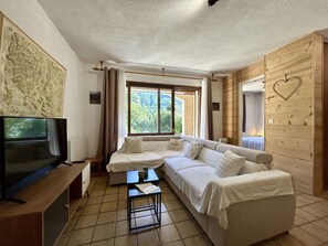 Una sala de estar moderna con sofá, televisor y ventana con vistas a zonas verdes.