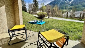 Una terrazza con due poltrone gialle e un tavolo, con vista su una strada e montagne.