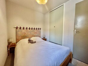 Ein Schlafzimmer mit Bett, Nachttisch, Lampe, Kleiderschrank und einer Tür.