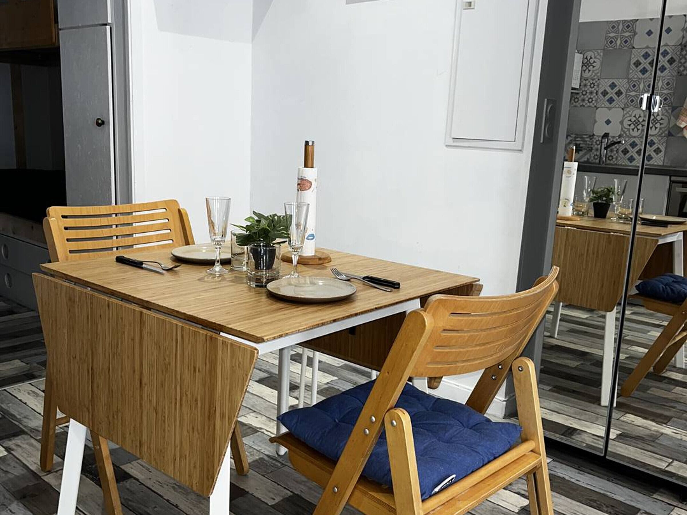 Een eetruimte met een houten tafel, stoelen en een spiegel die de keuken weerspiegelt.