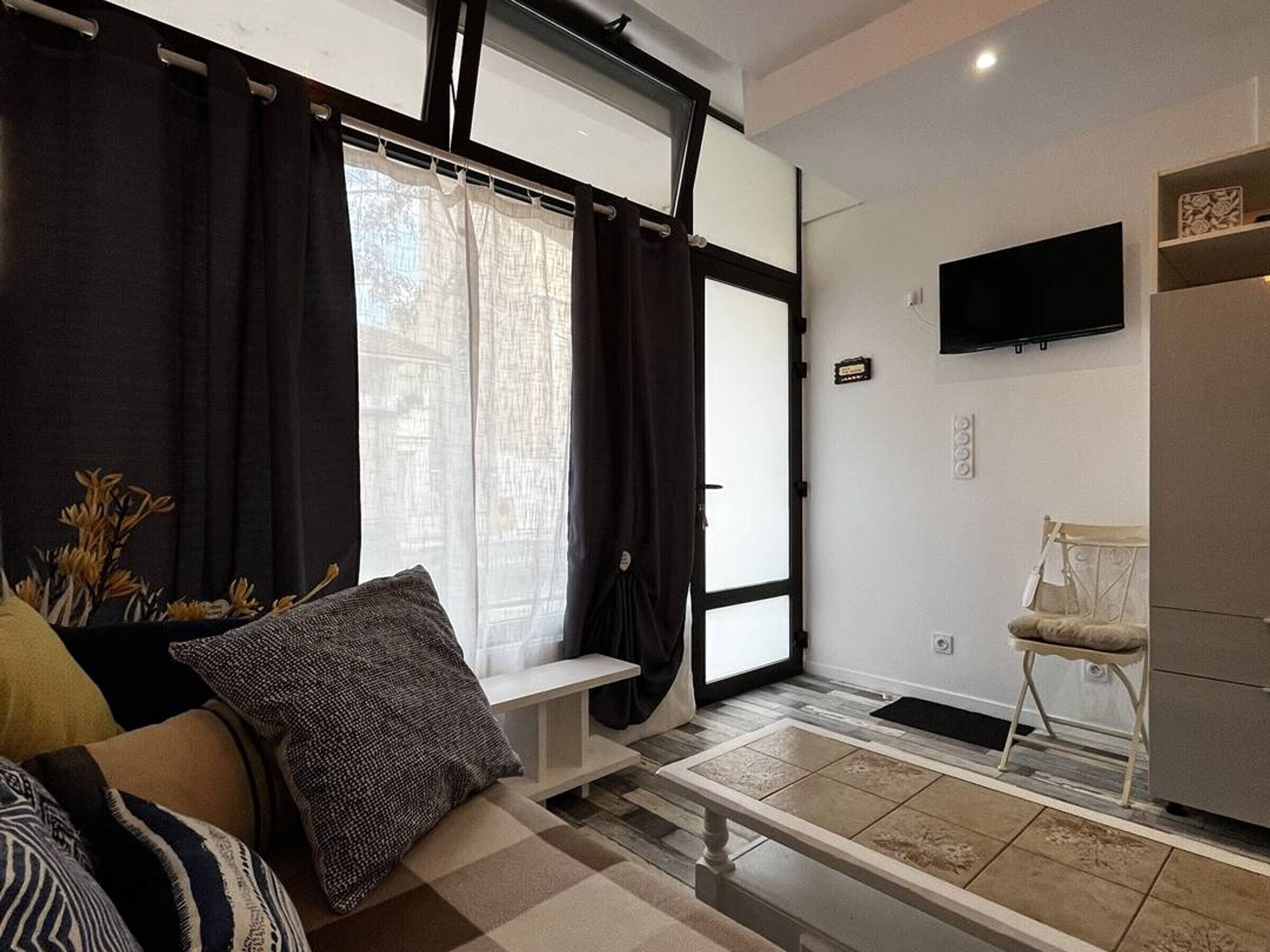 Un salon moderne comprenant un canapé, un banc, un fauteuil, un téléviseur à écran plat et une grande fenêtre avec des rideaux.