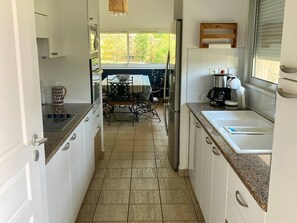 A narrow kitchen with white cabinets, a coffee maker, and a window. - Villa with private heated pool - 10 guests (Moliets-et-Maa)