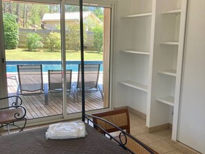 A room with a sliding glass door leading to a pool area, a bed with a mattress and pillows, and a white shelving unit. - Villa with private heated pool - 10 guests (Moliets-et-Maa)