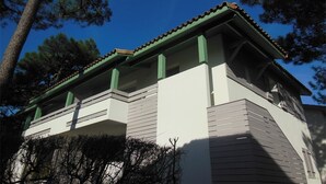 A two-story building with a balcony, green trim, and a tiled roof. - Comfortable apartment with parking - 8/10 guests (Moliets-et-Maa)