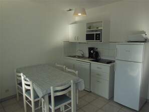 Una pequeña kitchenette con una mesa, sillas, un microondas, una cafetera y un refrigerador.