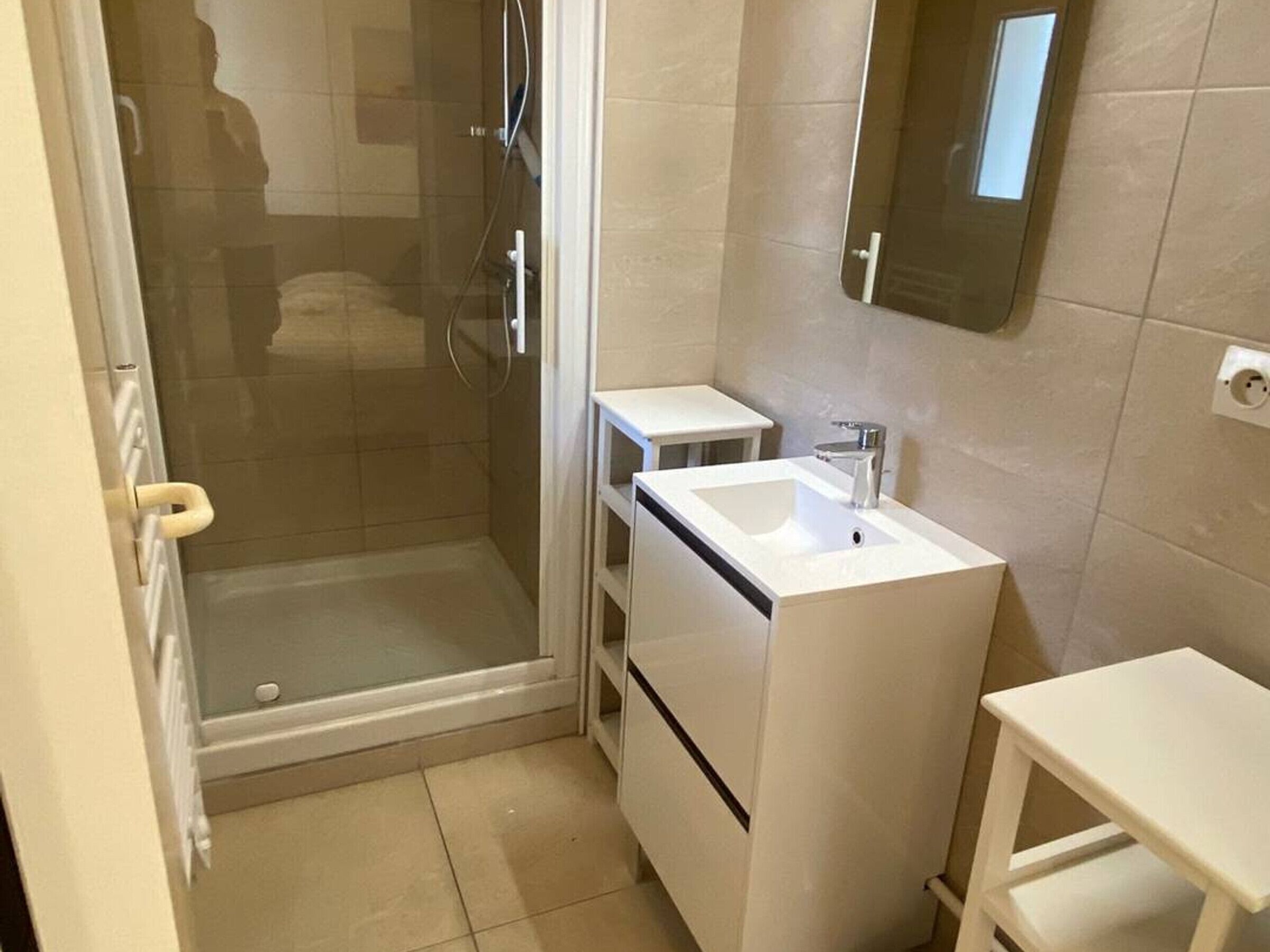 A small bathroom with a shower, a sink, and a mirror.