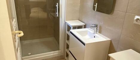 A small bathroom with a shower, a sink, and a mirror.