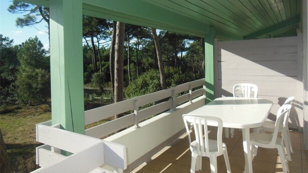 A covered outdoor area with a white table and chairs, a white bench, and a view of trees and grass. - Comfortable apartment with parking - 8/10 guests (Moliets-et-Maa)