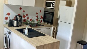 Ett litet, praktiskt kök med tvättmaskin, mikrovågsugn, liten ugn och diskho.