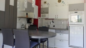 Uma cozinha moderna com armários brancos, micro-ondas, forno e um espaço de refeições com mesa e cadeiras redondas.