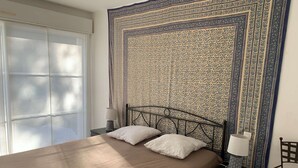 A bedroom with a large bed, two bedside tables, a chair, and a patterned tapestry on the wall. - Villa with pool - 10 guests (Moliets-et-Maa)