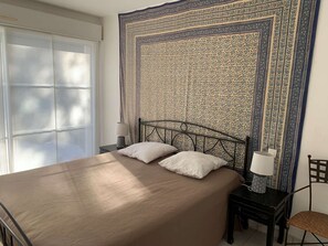A bedroom with a large bed, two bedside tables, a chair, and a patterned tapestry on the wall. - Villa with pool - 10 guests (Moliets-et-Maa)