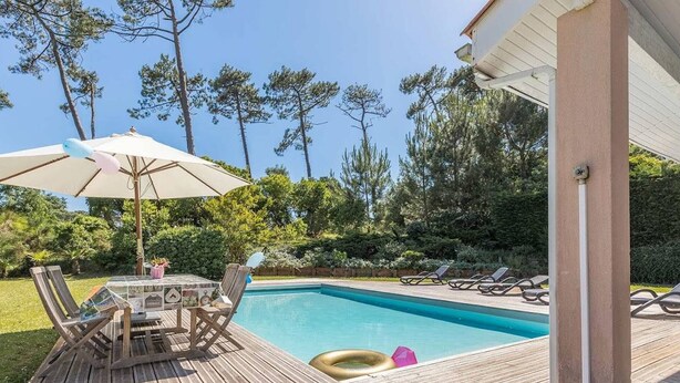 A wooden deck with a pool, lounge chairs, and a table with umbrellas. - Villa with pool - 10 guests (Moliets-et-Maa)