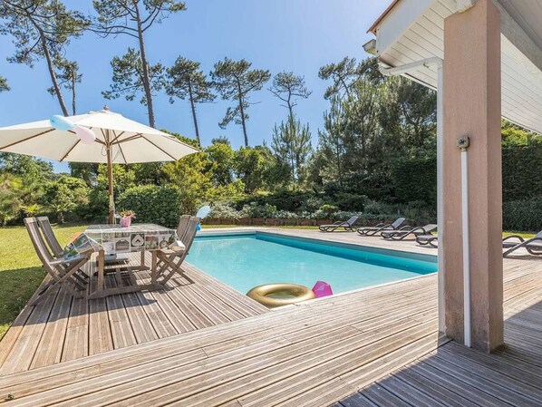 A wooden deck with a pool, lounge chairs, and a table with umbrellas. - Villa with pool - 10 guests (Moliets-et-Maa)