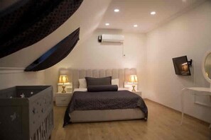 A bedroom with a bed, two bedside tables with lamps, a wall-mounted TV, and an air conditioning unit. - Nupelda Residence (İstanbul)