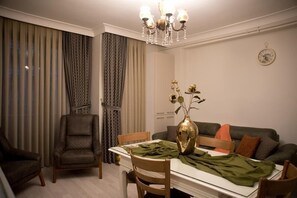 Un comedor con una mesa, sillas, un florero con flores, un sofá y cortinas.