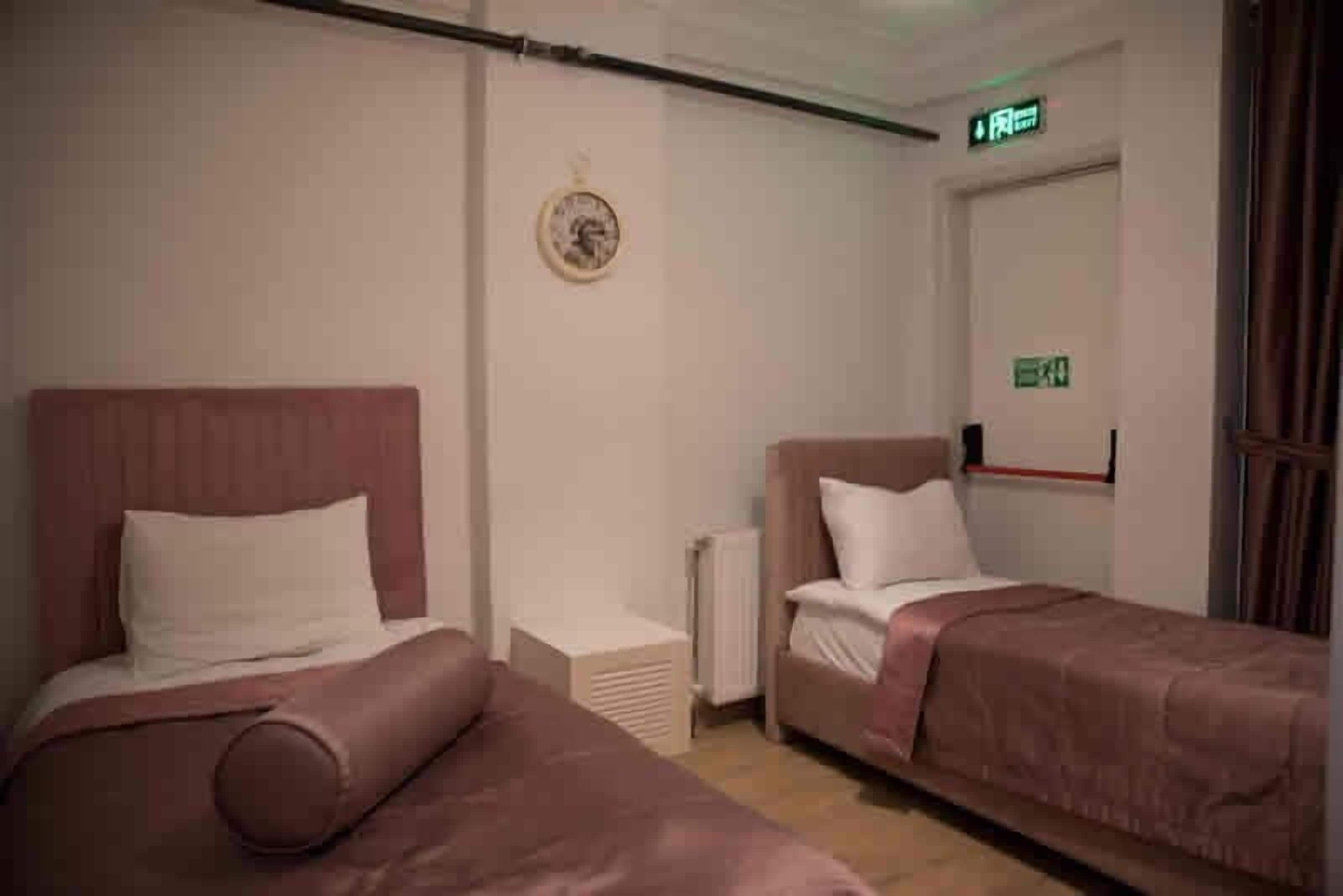 Et hotelværelse med to senge, en radiator, et vægur og et skilt med udgang.
