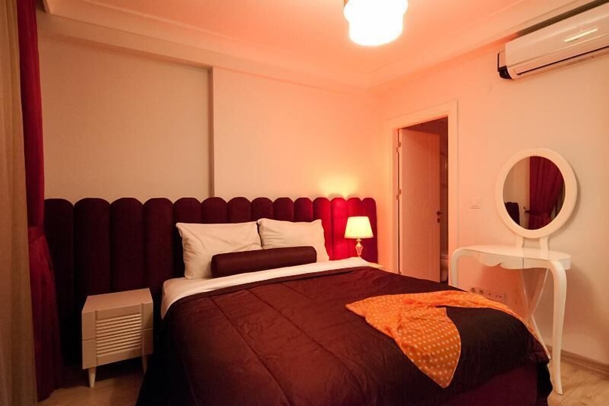 Un dormitorio con cama, mesita de noche, lámpara y espejo.