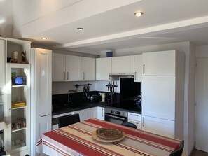 Eine kleine Küche mit weißen Schränken, einer schwarzen Arbeitsplatte und einer Tischdecke mit Streifen.